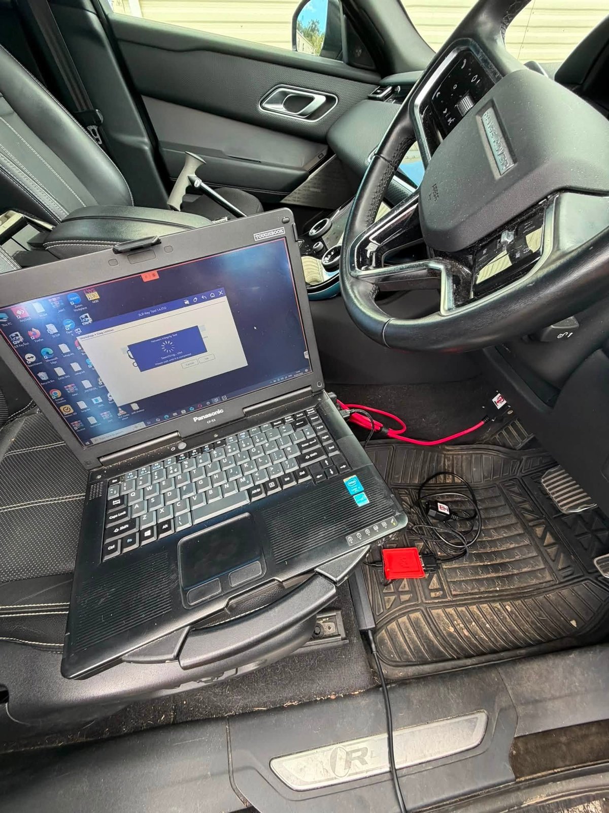 Laptop computer running diagnostic software inside a car interior with steering wheel and dashboard visible